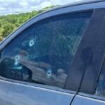 Veículo branco com marcas de perfuração de bala no para-brisa e portas na Praia do Abaís, em Estância.