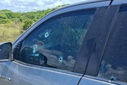 Veículo branco com marcas de perfuração de bala no para-brisa e portas na Praia do Abaís, em Estância.