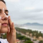 Pessoa aplicando protetor solar no rosto sob céu nublado e luz difusa de mormaço em Aracaju.