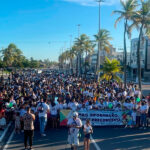 Participantes da 4ª Caminhada de Conscientização do Autismo em Aracaju segurando cartazes azuis na Orla de Atalaia.