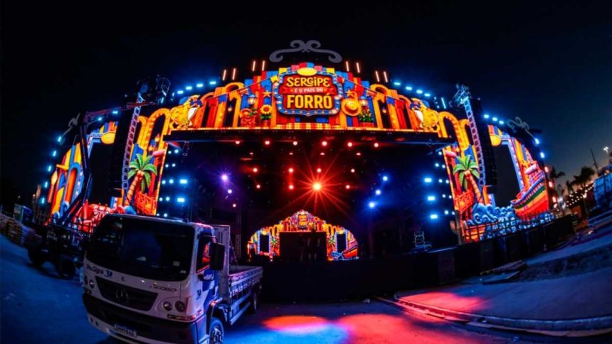 Portal de entrada estruturado do Arraiá do Povo na Orla de Atalaia com equipes de segurança realizando revistas e controle de público.