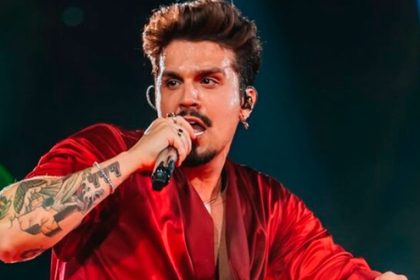 Cantor sertanejo Luan Santana sorrindo com os braços abertos em um palco iluminado por refletores durante um grande show musical.