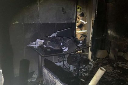 Interior de um cômodo residencial danificado pelo fogo, com paredes manchadas de fuligem e restos de tecidos queimados.