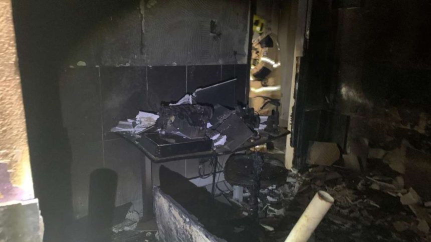 Interior de um cômodo residencial danificado pelo fogo, com paredes manchadas de fuligem e restos de tecidos queimados.