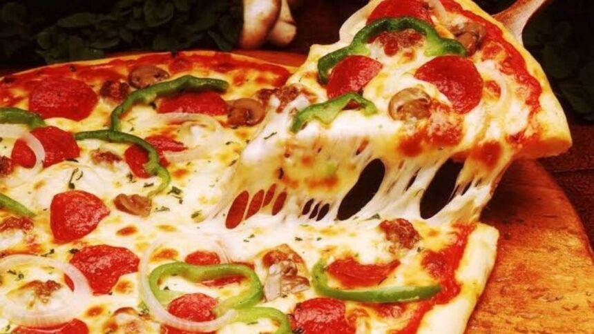 Pizza fatiada em uma mesa de restaurante com calculadora e notas de dinheiro ao lado.