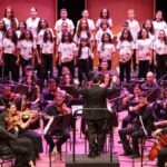 Músicos da Orquestra Jovem de Sergipe tocando instrumentos sinfônicos no palco do teatro.