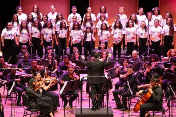 Músicos da Orquestra Jovem de Sergipe tocando instrumentos sinfônicos no palco do teatro.